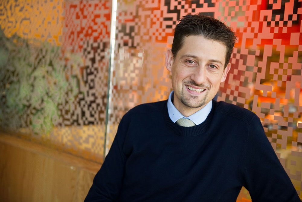 Male faculty member standing in front of a colourful chekered glass wall, MIT