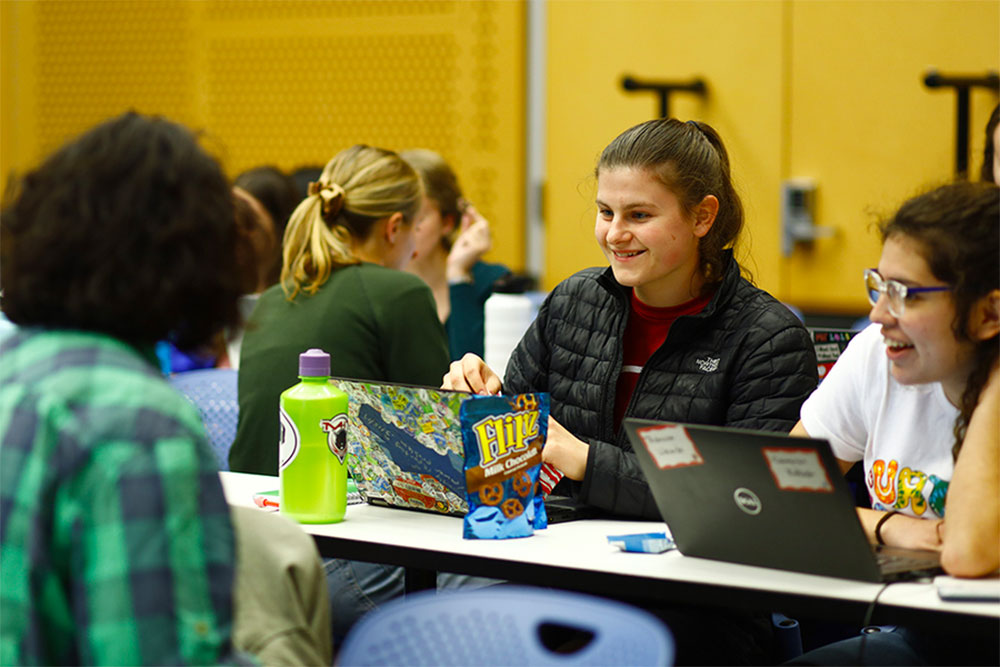 Several MIT students sitting at a narrow table collaborate in a classroom