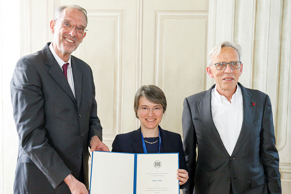 three people standing in a row, tall male on left, female holding certificate in the middle, medium height male on left