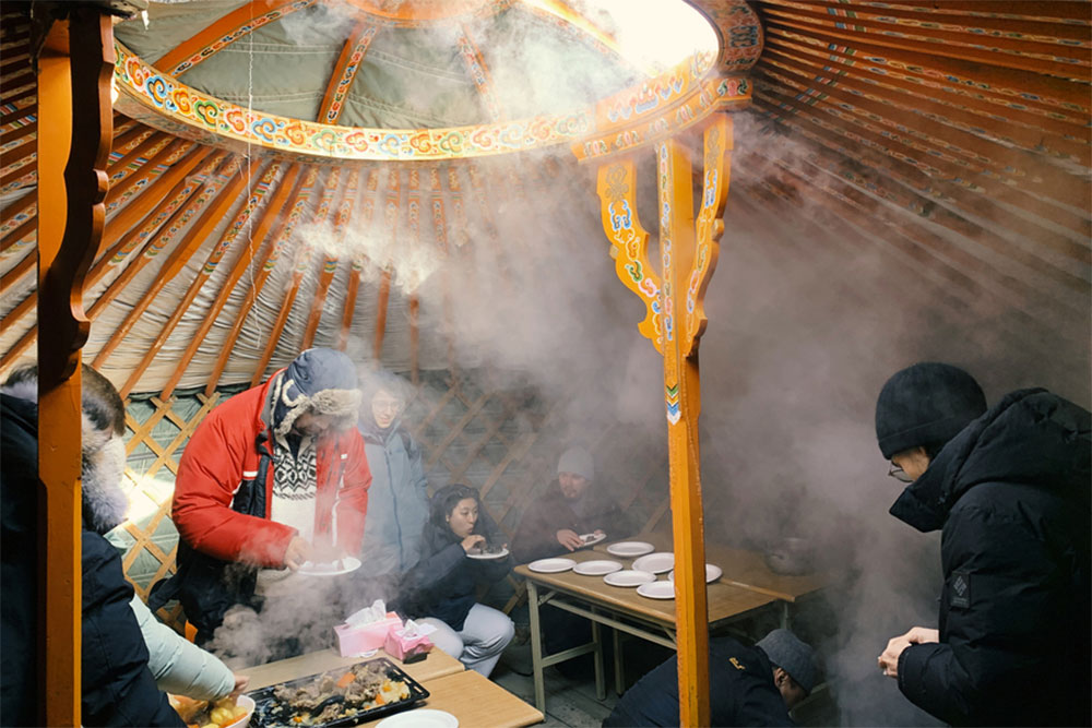 Students dressed for cold weather enjoy a meal inside a space filled with with warm steam