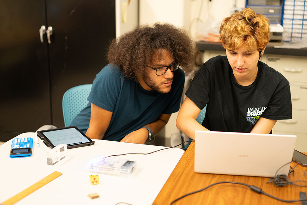 two students at a table in a lab looking at a computerscreen together