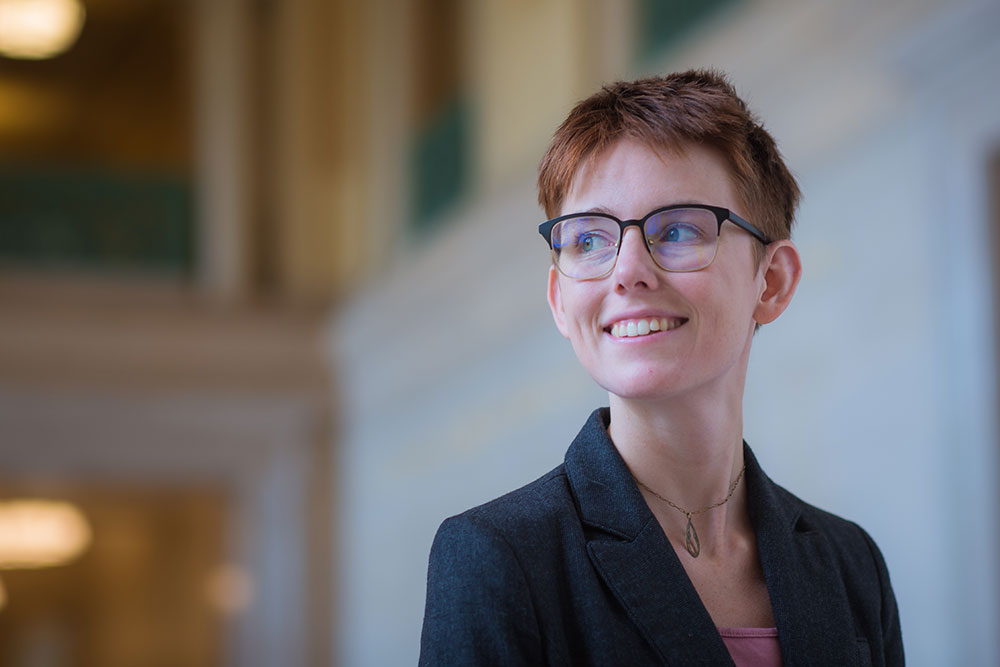 Headshot of grad student Amelia Trainer standing inside a lobby of an MIT building, background in soft focus, MIT