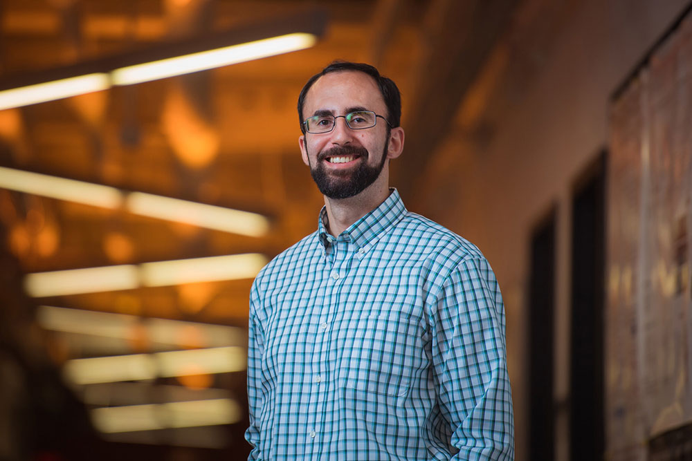 Male faculty member Koroush Shirvan in a hallway with lights overhead in a zig-zag pattern, MIT