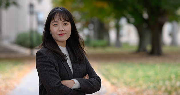 Female grad student Youyeon Choi, arms folded outside on a path with trees on the right, MIT